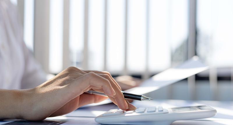 A business woman using a calculator to calculate numbers on a companys financial documents she is analyzing historical financial data to plan how to grow the company. Financial concept
