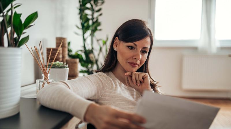 Pensive woman looking at received mail at home holding blank envelopes
