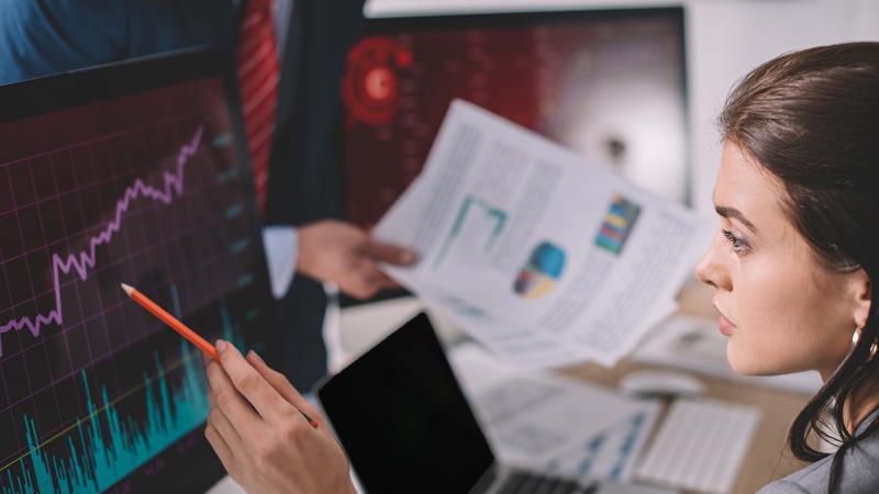 Selective focus of information security analyst pointing on charts on computer monitor near colleague with papers isolated on grey